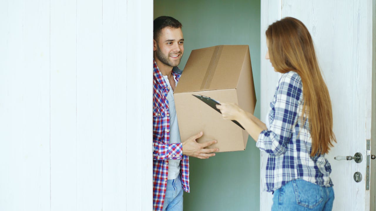 Two people exchanging a cardboard box at the door, representing delivery service.